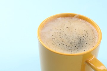 Aromatic coffee in cup on light blue background, closeup. Space for text