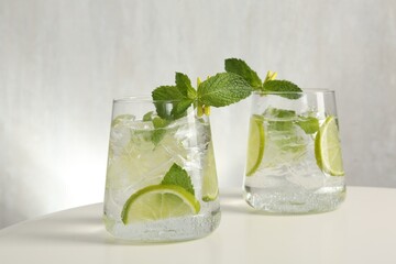 Tasty cocktail with lime and ice cubes on white table, closeup