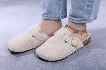 Woman in stylish white slippers on grey textured floor, closeup
