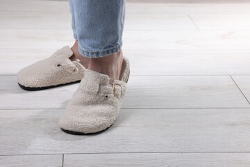 Woman in soft white slippers on light wooden floor, closeup. Space for text