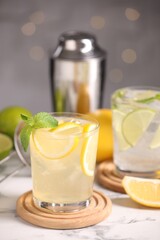 Tasty citrus cocktails in glasses on white marble table against blurred lights, closeup