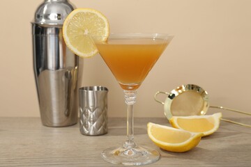 Tasty lemon cocktail in glass and bartender equipment on wooden table against beige background,...