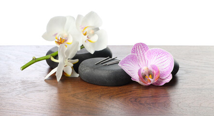 Acupuncture needles, orchid flowers and spa stones on wooden table against white background