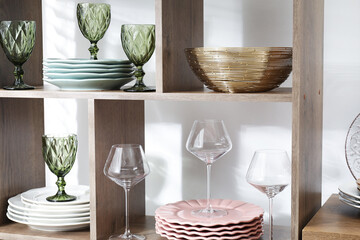 Shelving unit with different dishware and glasses near white wall indoors