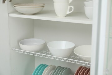 Clean dishware and cups on shelves in cabinet indoors