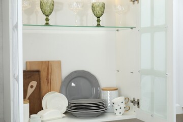 Clean dishware, cups and glasses on shelves in cabinet indoors