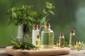 Bottles of essential oils and different herbs on wooden table outdoors, closeup