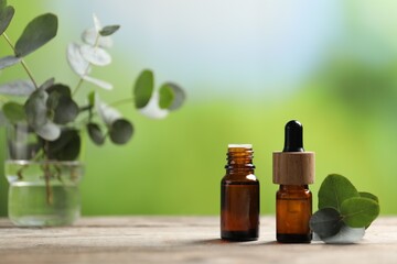 Bottles of essential oils and eucalyptus branches on wooden table outdoors, closeup. Space for text