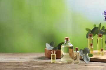 Bottles of essential oils and eucalyptus leaves on wooden table outdoors, space for text