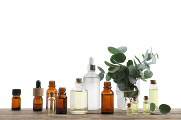 Bottles of essential oils and eucalyptus branches on wooden table against background