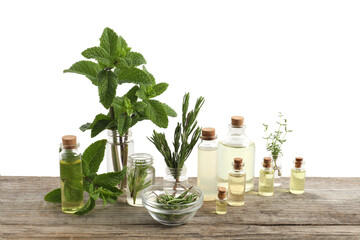 Bottles of essential oils and different herbs on wooden table against white background