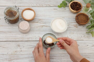 Making natural scrub. Woman adding sugar into jar at white wooden table, top view