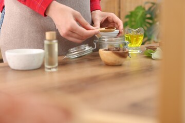 Making natural scrub. Woman adding coffee into jar at wooden table, closeup