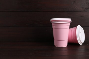 Set of disposable cups on wooden table, space for text