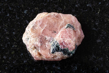 sample of raw pink ruby mineral on black granite