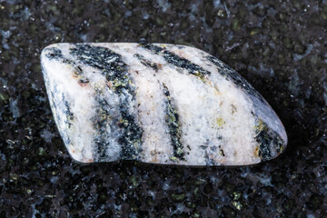 sample of tumbled gneiss mineral on black granite