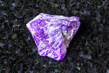 sample of raw sugilite mineral on black granite