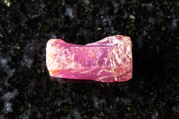 sample of rough pink ruby crystal on black granite