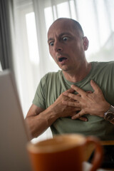 Close-up of man having sudden chest pain while working on laptop at home, health emergency in home...