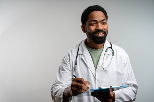 Smiling African doctor writing on clipboard while analyzing medical results, professional portrait on isolated background - Powered by Adobe