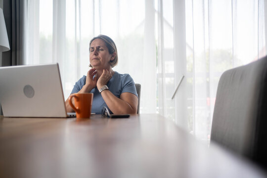 Woman with sore throat or thyroid problem working from home on laptop, health issue in home office setting