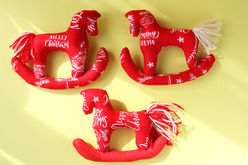 Three red horses sewn from fabric. Concept - New Year's tree toy, handmade in Tilda style. Yellow background, sun glare.