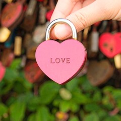 Hand holding a heart-shaped padlock inscribed with "LOVE," blurred background of similar locks
