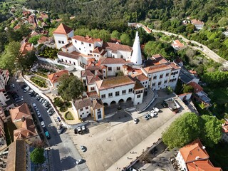 Aerial drone footage showing the historic town of Sintra and the National Palace of Sintra, with red rooftops, green hills, and traditional architecture captured during daylight.