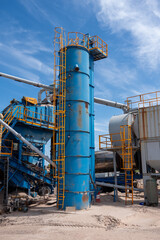 Tall blue industrial silo with yellow ladders at asphalt mixing plant under blue sky. concept of construction site work