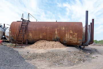 Abandoned industrial oil tank with rusted surface on construction site.