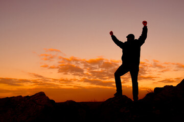 the silhouette of a man holding his hands up celebrating the victory of climbing and overcoming