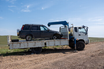 Broken SUV being loaded onto tow truck on rural dirt road under blue sky. Concept of roadside assistance