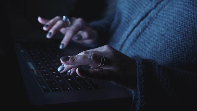 Woman's hands typing on a laptop keyboard, low-light footage