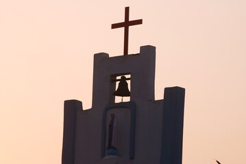 Campanile bianco con croce e campana al tramonto rosa.
