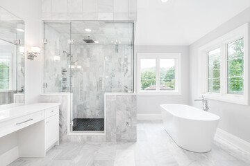 A luxurious bathroom with a freestanding tub, white vanity, and a glass walk-in shower with marble tiles and bench seat.