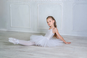 A young ballerina in white tutu and pointe ballet shoes with flower sits on the floor in the...