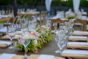 Wooden table decorated with crystal glasses and floral centerpiece, set outdoors for a wedding or...