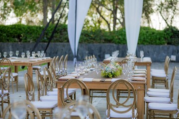 Wooden table decorated with crystal glasses and floral centerpiece, set outdoors for a wedding or...
