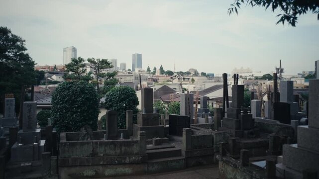 Japanese Cemetery Overlooking Cityscape on Sunny Day &ndash; Traditional graves in Japan with urban city skyline in the background under bright sunlight.