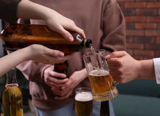 Woman pouring beer into her friend's glass indoors, closeup