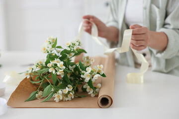 Woman making bouquet of jasmine branches at white table, closeup