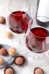 Delicious truffle bonbons and red wine on light grey background, closeup