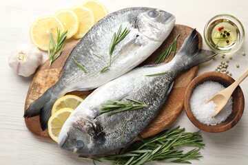 Fresh raw dorado fish, lemon slices, rosemary and spices on white wooden table, flat lay. Organic seafood