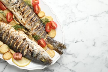 Tasty roasted seabass fish served with potatoes, tomatoes and lemon on white marble table, top view and space for text. Homemade seafood dish