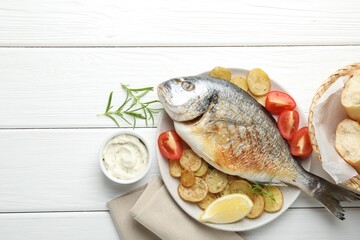 Homemade seafood dish. Tasty roasted dorado fish served with vegetables and sauce on white wooden table, flat lay. Space for text