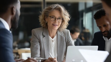 mature older ceo businesswoman mentor in glasses negotiating growth business plan with diverse executive managers at boardroom meeting table using laptop multicultural team work together in office no