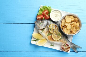 Homemade seafood dish. Tasty roasted dorado fish served with vegetables and sauce on light blue wooden table, flat lay. Space for text