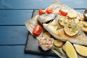 Homemade seafood dish. Tasty roasted dorado fish with vegetables and spices on blue wooden table, closeup. Space for text