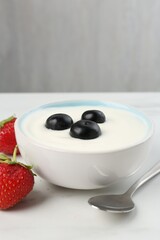 Tasty yoghurt with blueberries and strawberries in bowl on white marble table, closeup