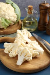 Pieces of cauliflower, knife and spices on blue wooden table, closeup